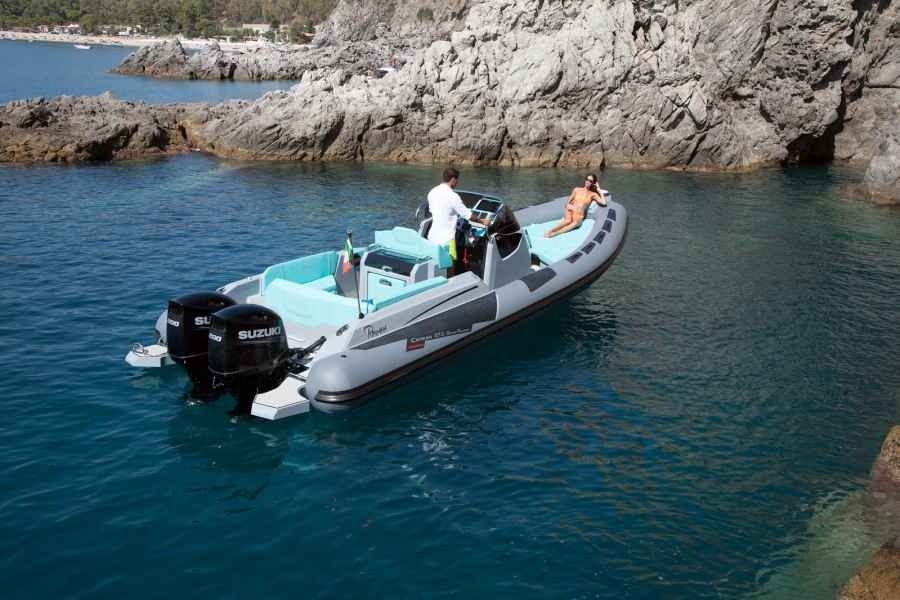 Small gray motorboat with two people on turquoise water near rocky cliffs