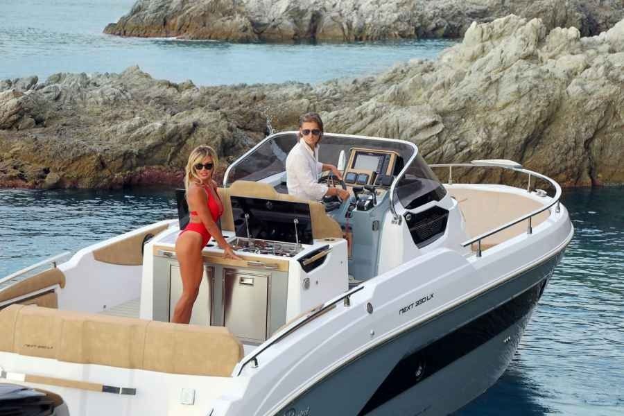 Two people on a white Ranieri next 330 speedboat near rocky coastline, one steering and one standing by the helm