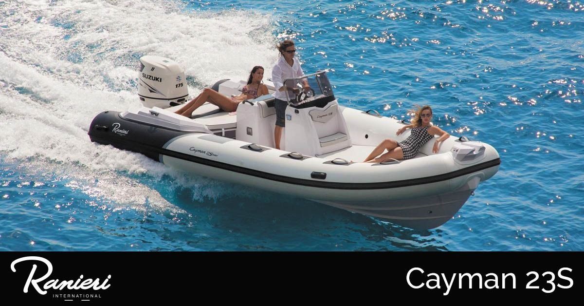 People relaxing on a white-and-black inflatable boat speeding across blue water, labeled Cayman 23S.