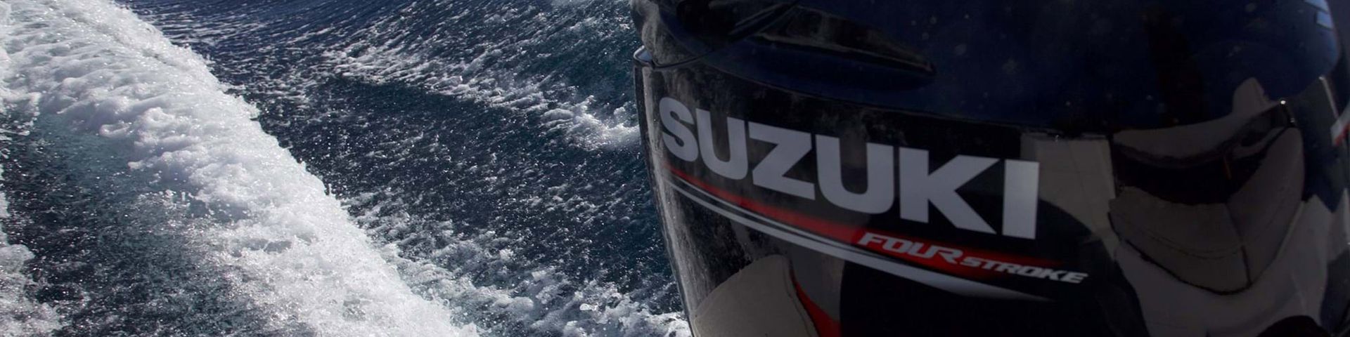 Close-up of a Suzuki outboard motor cutting through choppy water, with spray trailing behind.