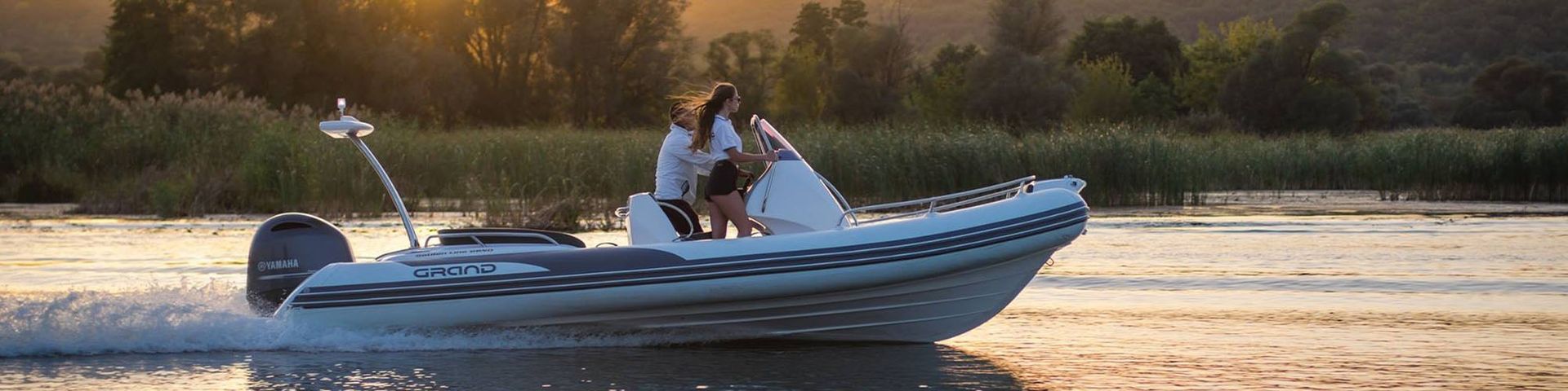 Two people in a small motorboat on a calm lake at sunset, with trees in the background