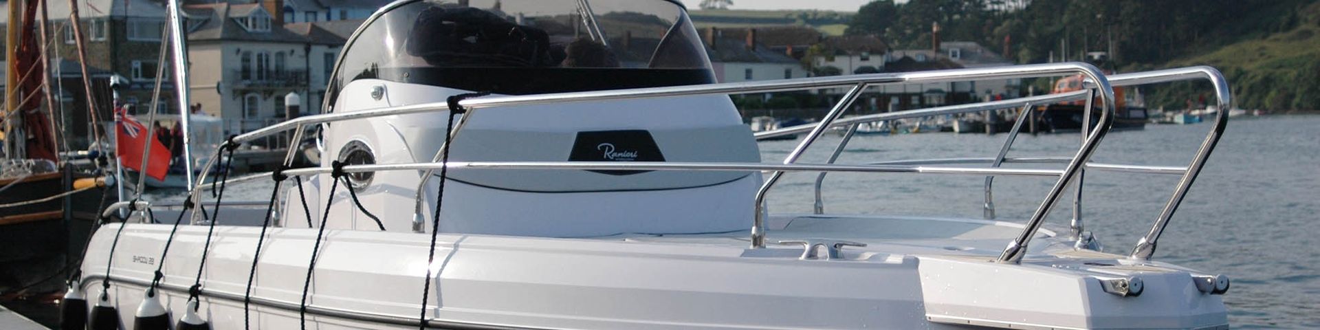 White yacht docked in a marina, with railings and calm water in the foreground.