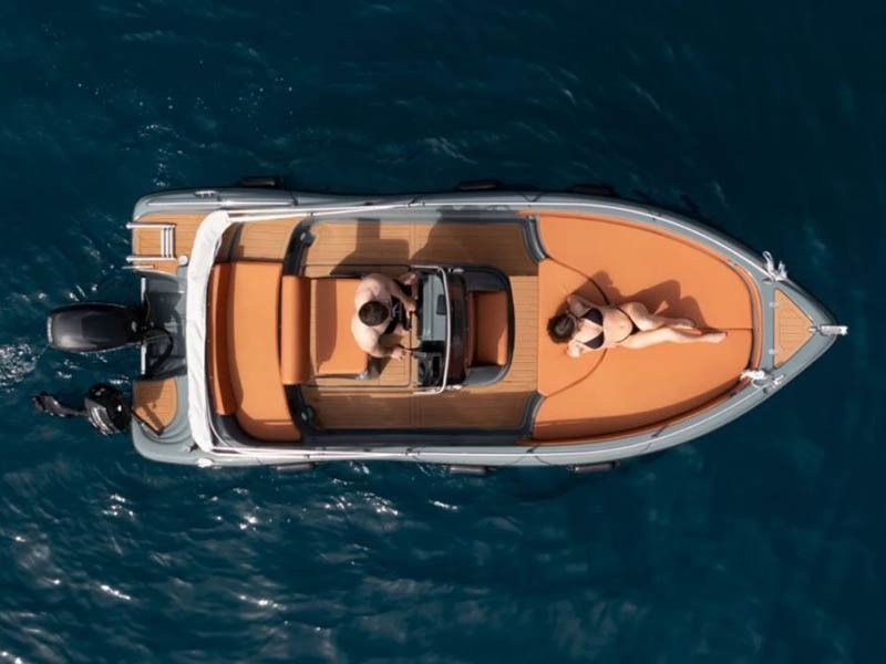 Aerial view of a small orange motorboat cruising on dark blue water with two people aboard