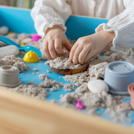 Hands playing in gray kinetic sand on a blue tray with small molds and colorful toy cups — Sorrento Valley Children's Center Hands playing in gray kinetic sand on a blue tray with small molds and colorful toy cups — Sorrento Valley Children's Center