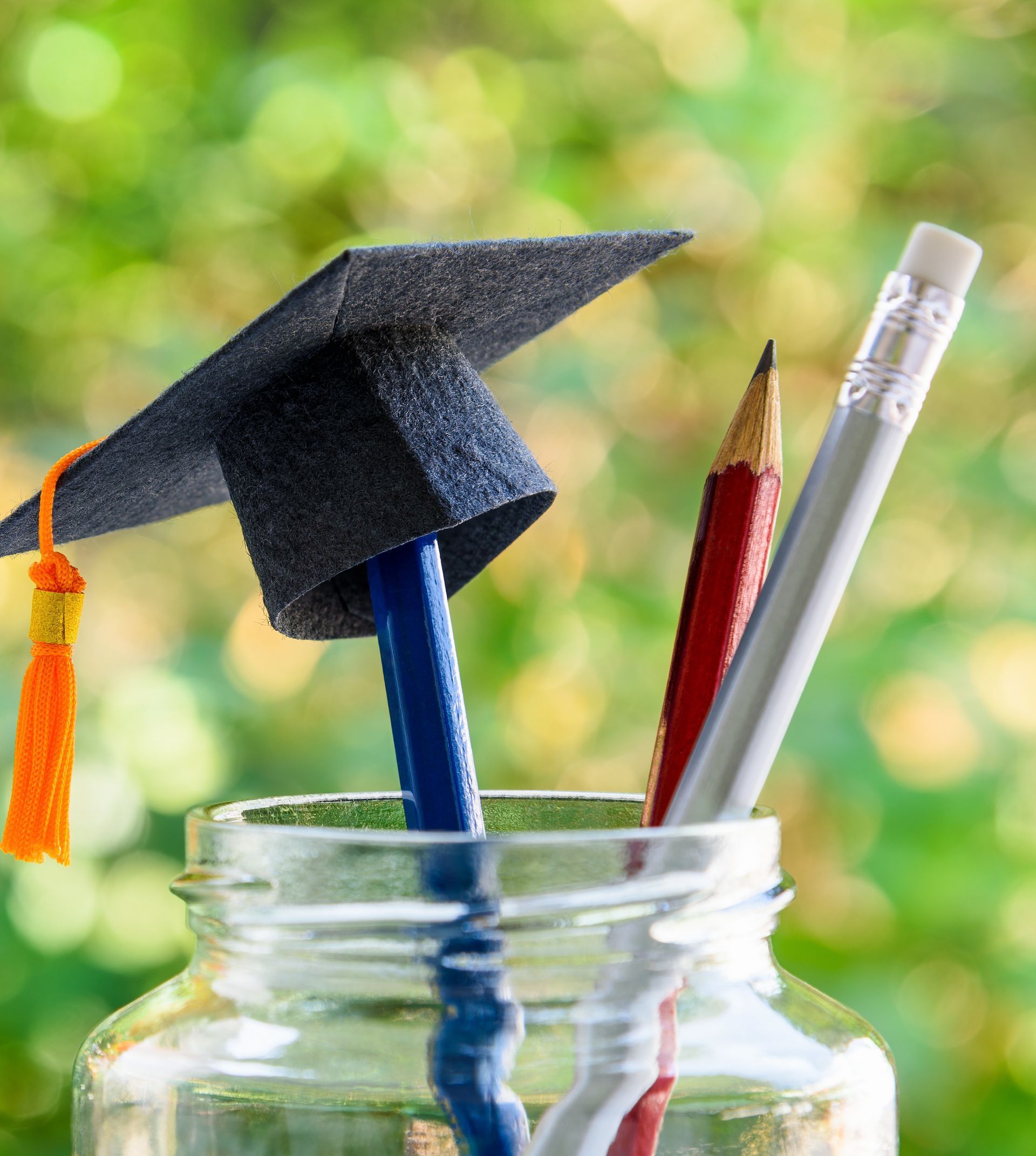 Green apple beside a cup of colored pencils and rulers on a wooden desk, with a chalkboard background Graduation cap in a glass jar with pencils, set against a blurred green background