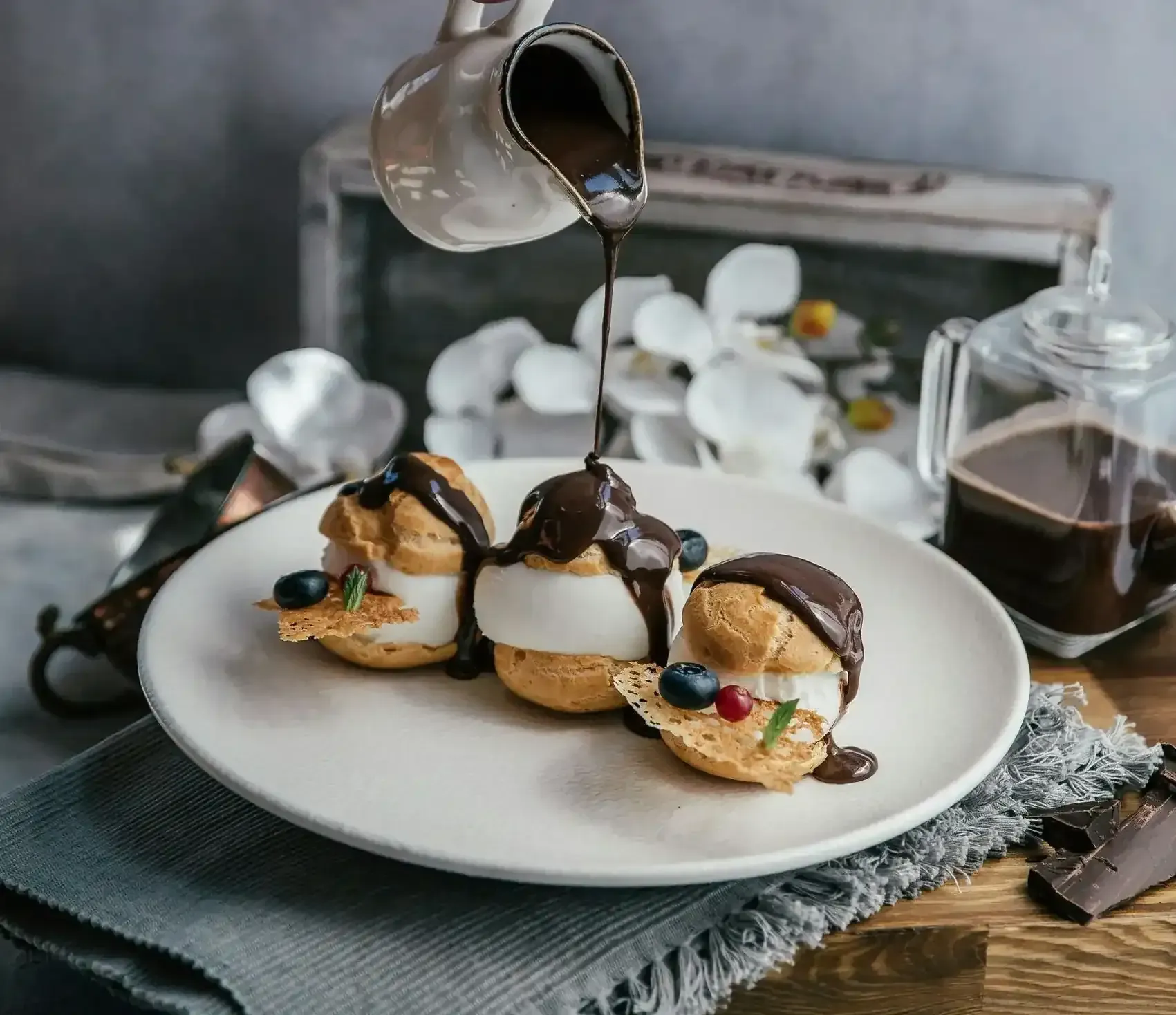 three profiteroles being drenched with chocolate syrup