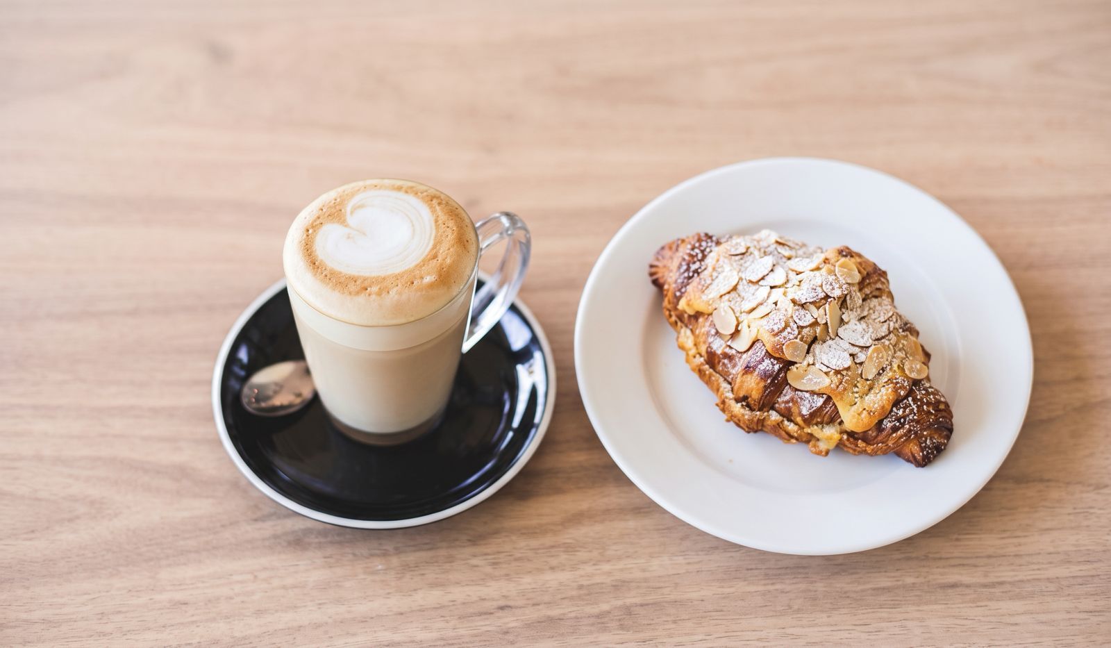 a cup of latte in a clear mug and a twice-baked almond croissant