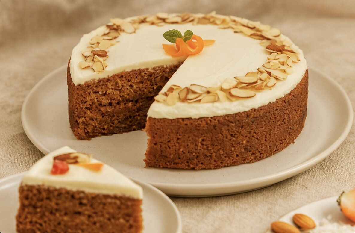 sliced dairy free carrot cake with white frosting on ceramic plate warm linen background and almond topping