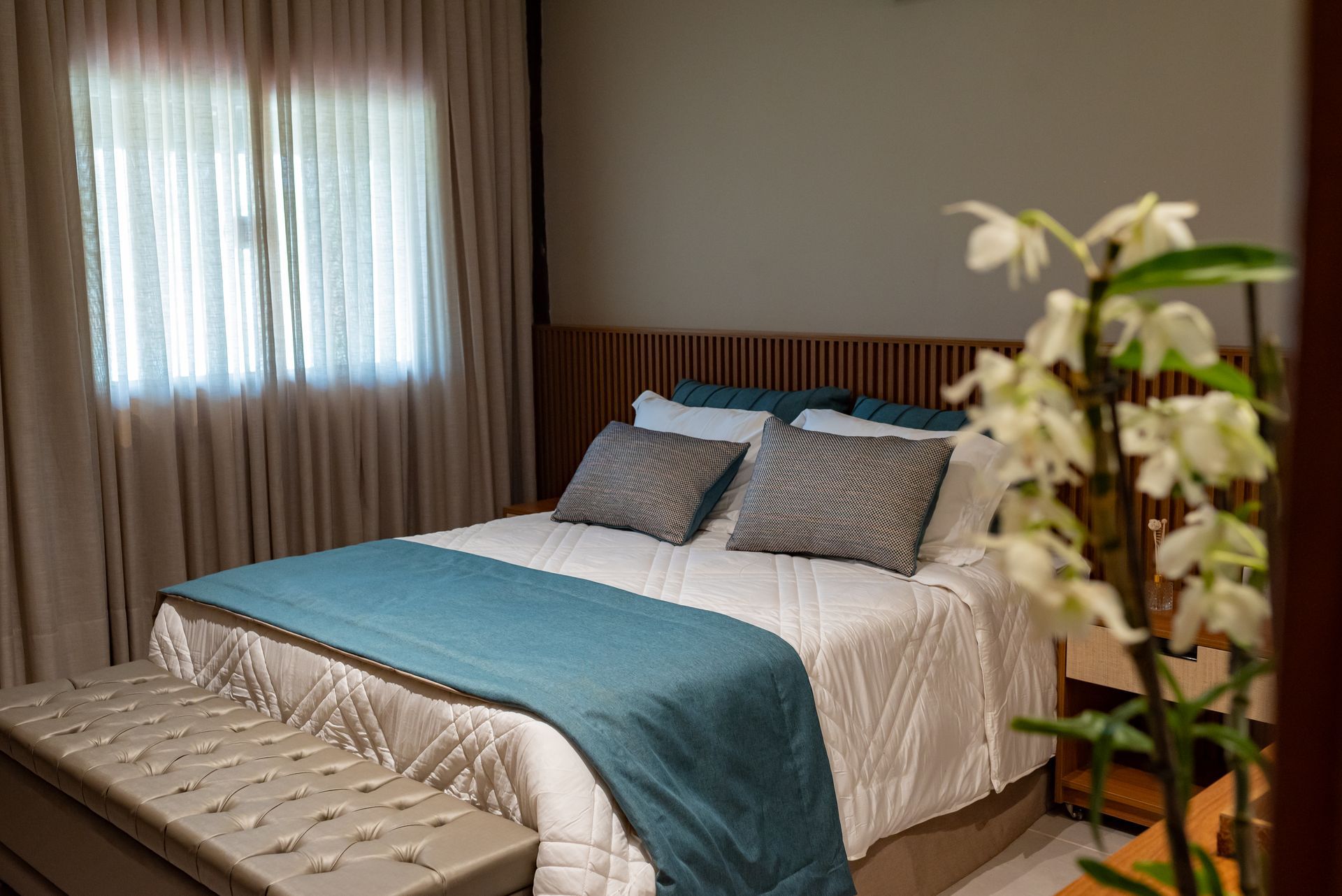 Um quarto com cama, janela, banco e flores.