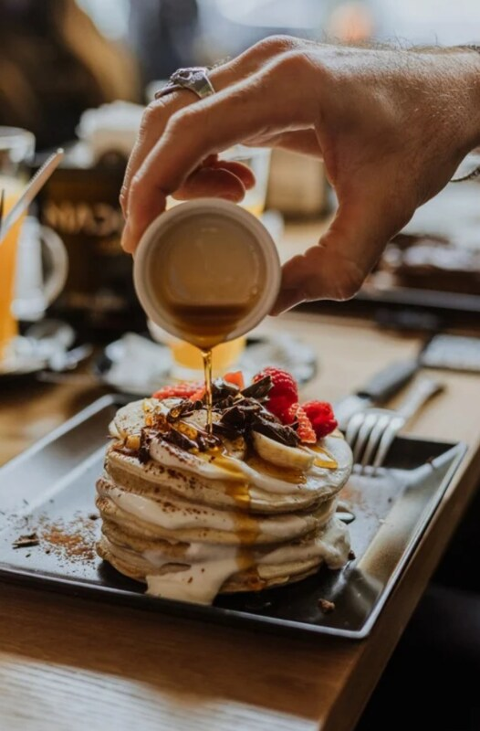 Sciroppo versato a mano su pancake impilati con frutta e cioccolato.