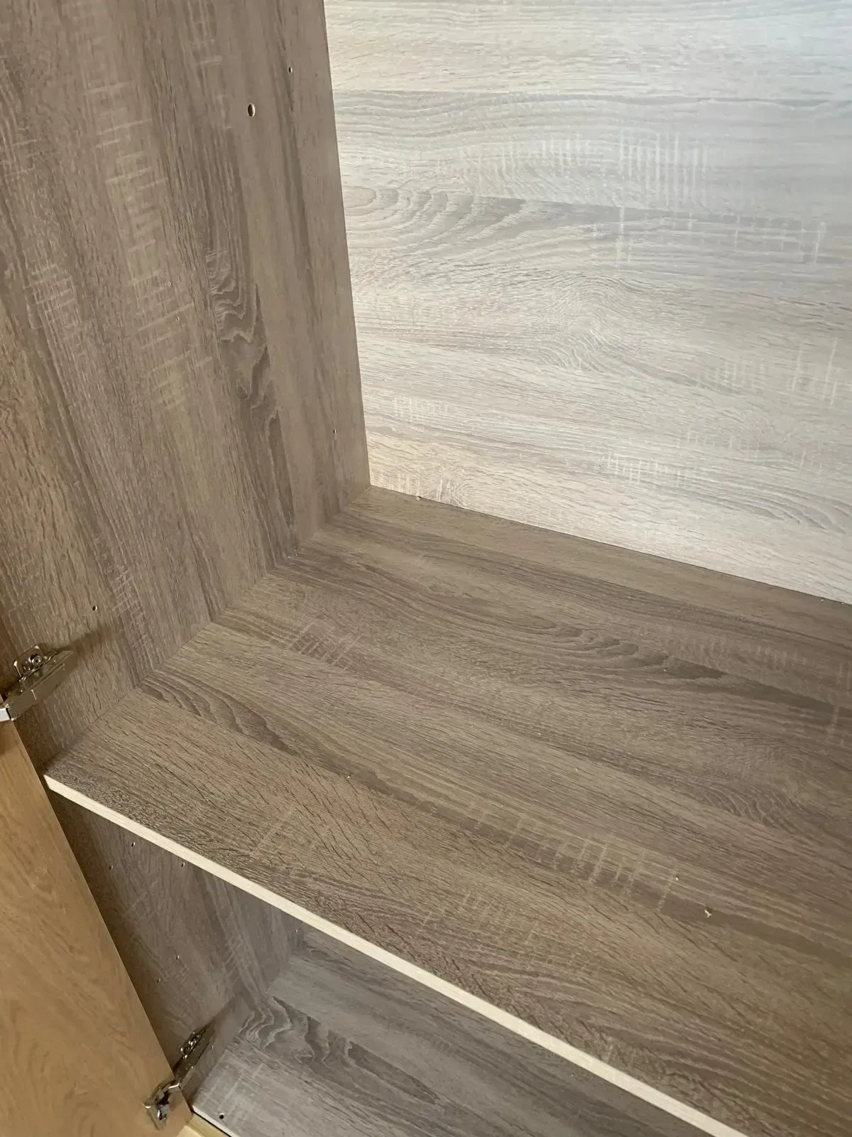 Wood-grain cabinet interior with a white shelf and a metal hinge visible.