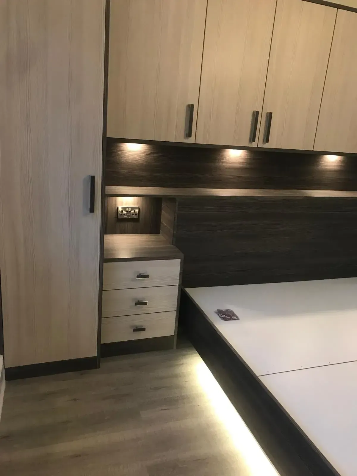 Modern bedroom with built-in wood cabinets, bedside drawers, and a bed with white bedding under warm lights
