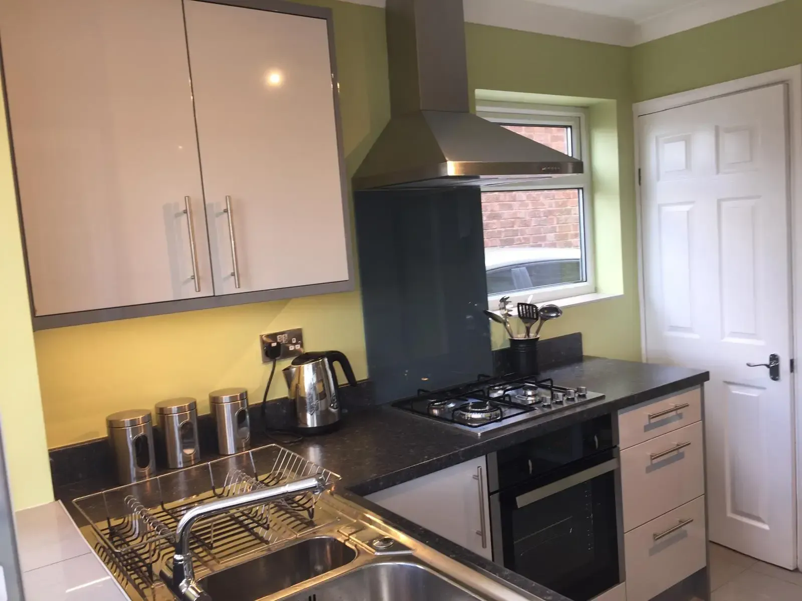 Modern L-shaped kitchen with light gray cabinets, white countertops, black oven and hood, and a farmhouse sink.