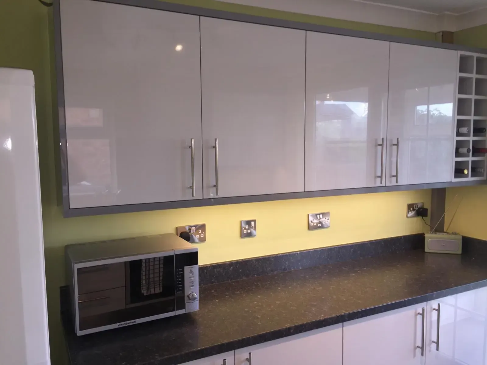 Modern kitchen counter with glossy white cabinets, black countertop, microwave, and under-cabinet lighting.