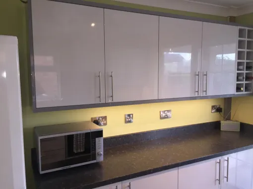 Modern kitchen with white cabinets, dark countertop, microwave, and green wall trim.
