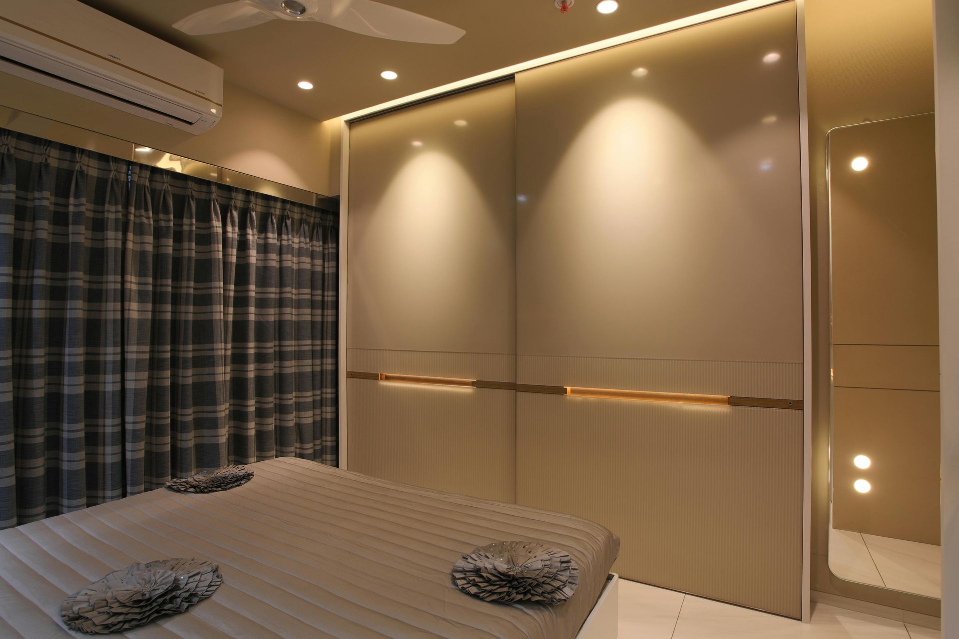 Modern bedroom with a large bed, blue curtains, and warm recessed lighting on a mirrored wall.