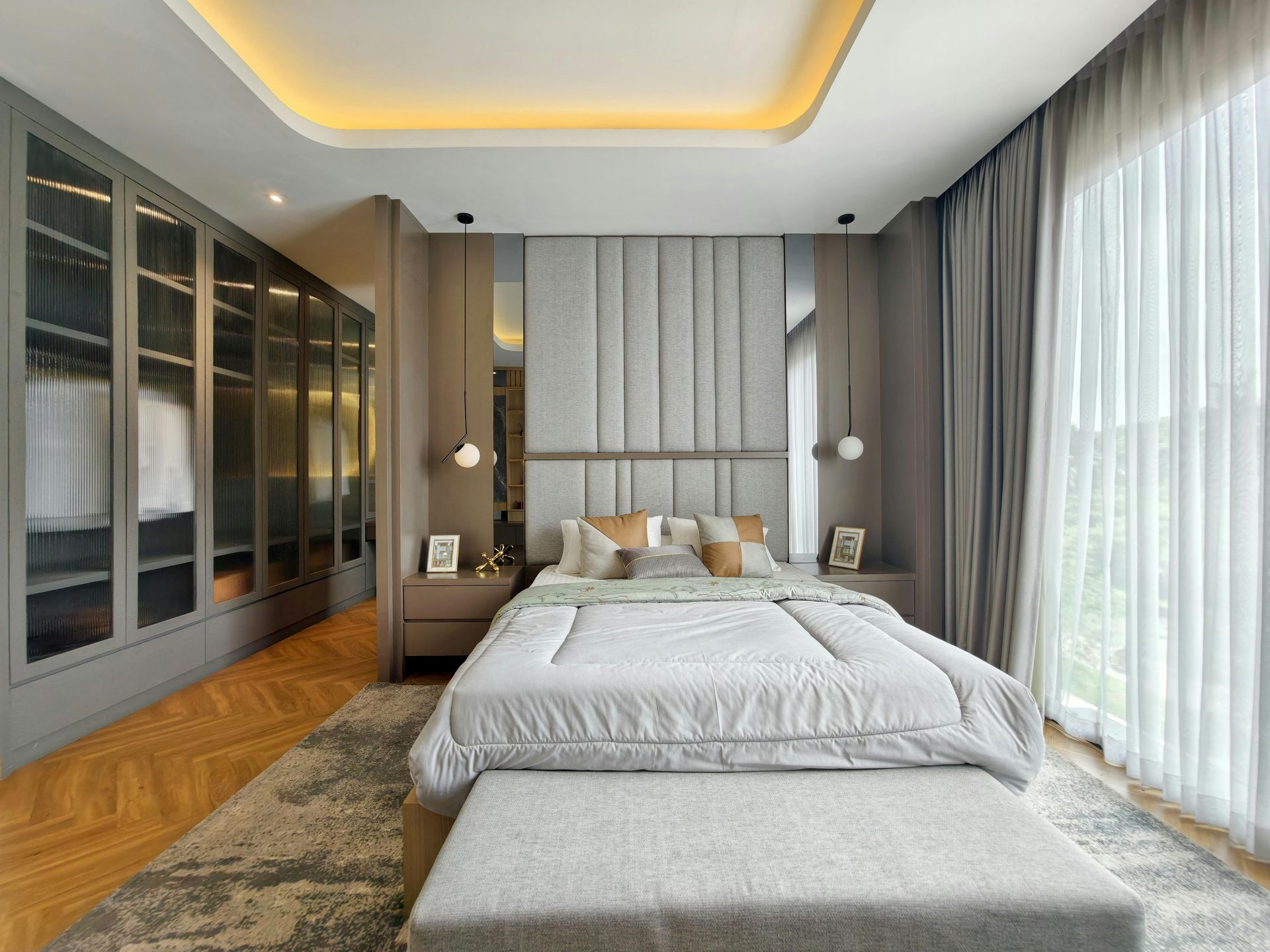 Modern bedroom with a bed, gray bench, wood floor, mirrored wardrobe, and sheer curtains by a bright window