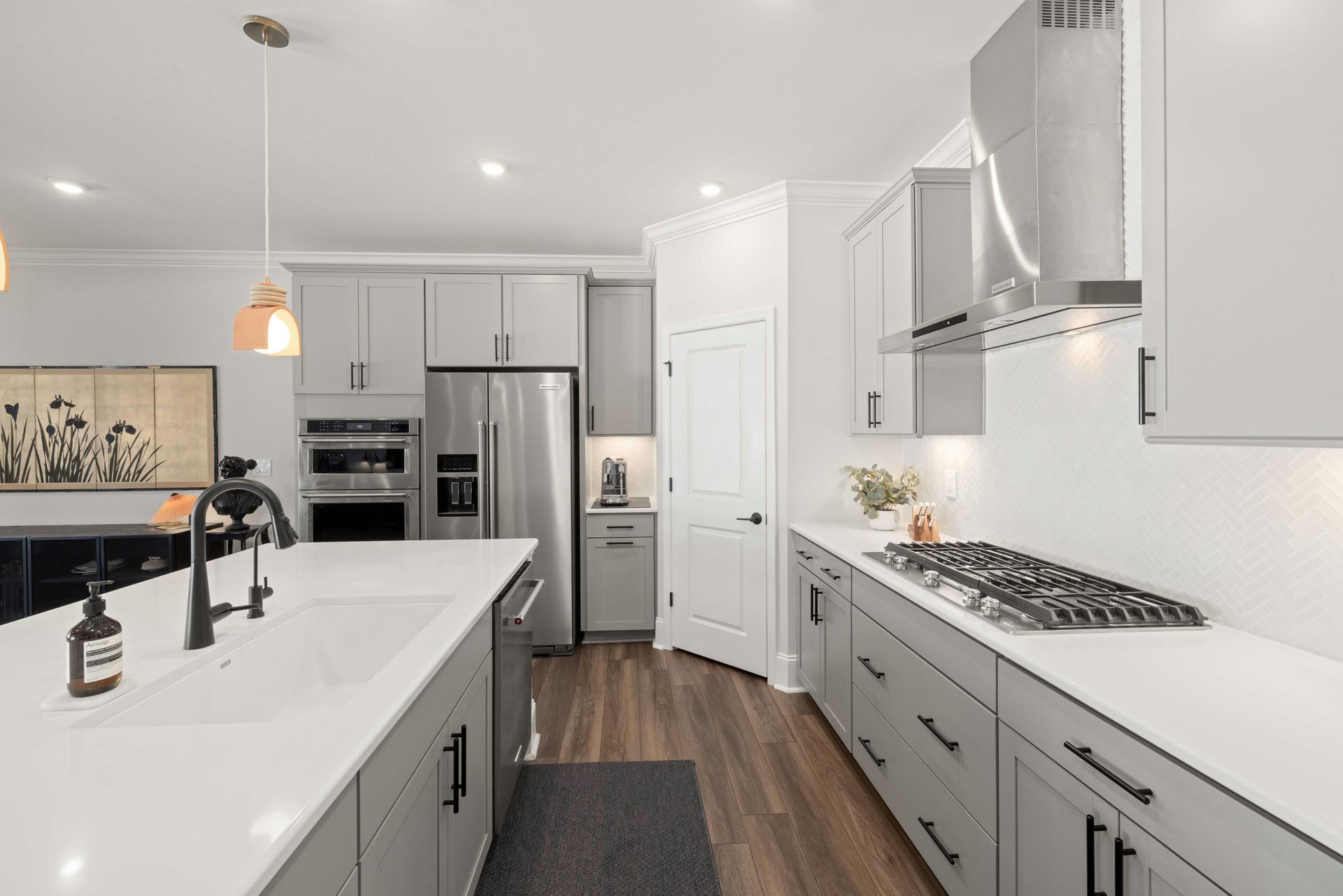 Modern L-shaped kitchen with light gray cabinets, white countertops, black oven and hood, and a farmhouse sink.