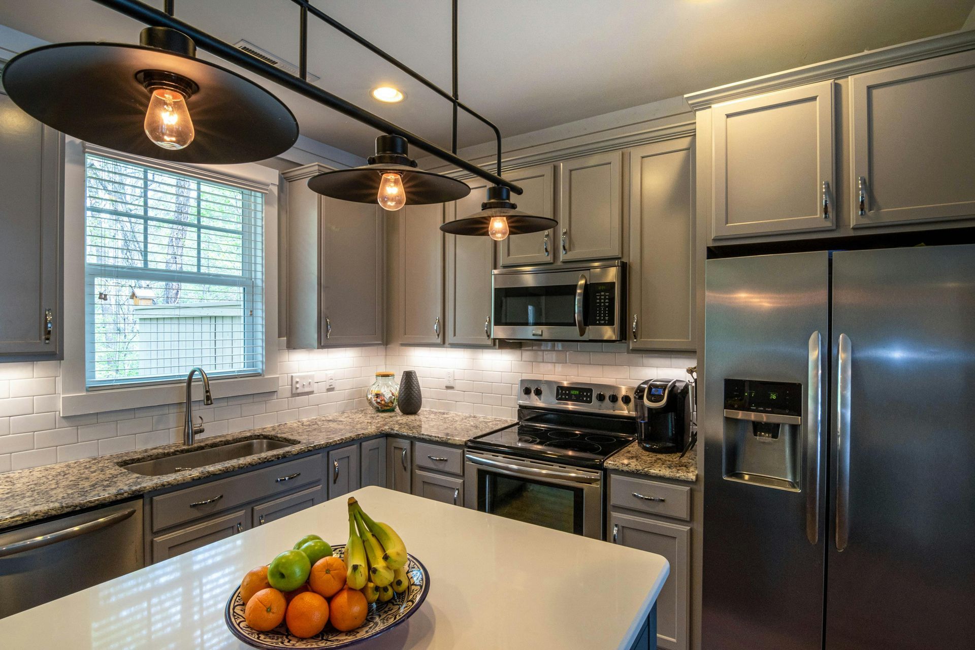 Modern L-shaped kitchen with light gray cabinets, white countertops, black oven and hood, and a farmhouse sink.