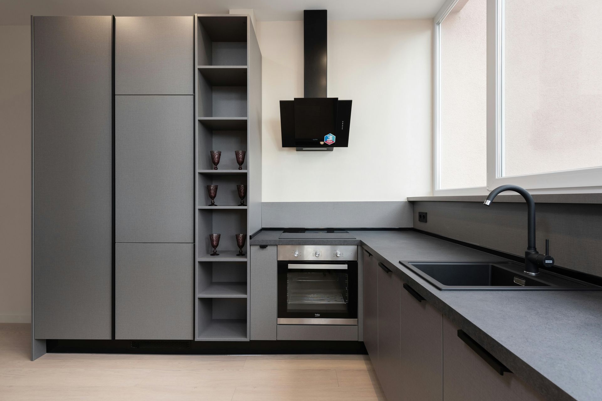 Modern gray kitchen with built-in oven, open shelving, black fixtures, and large windows