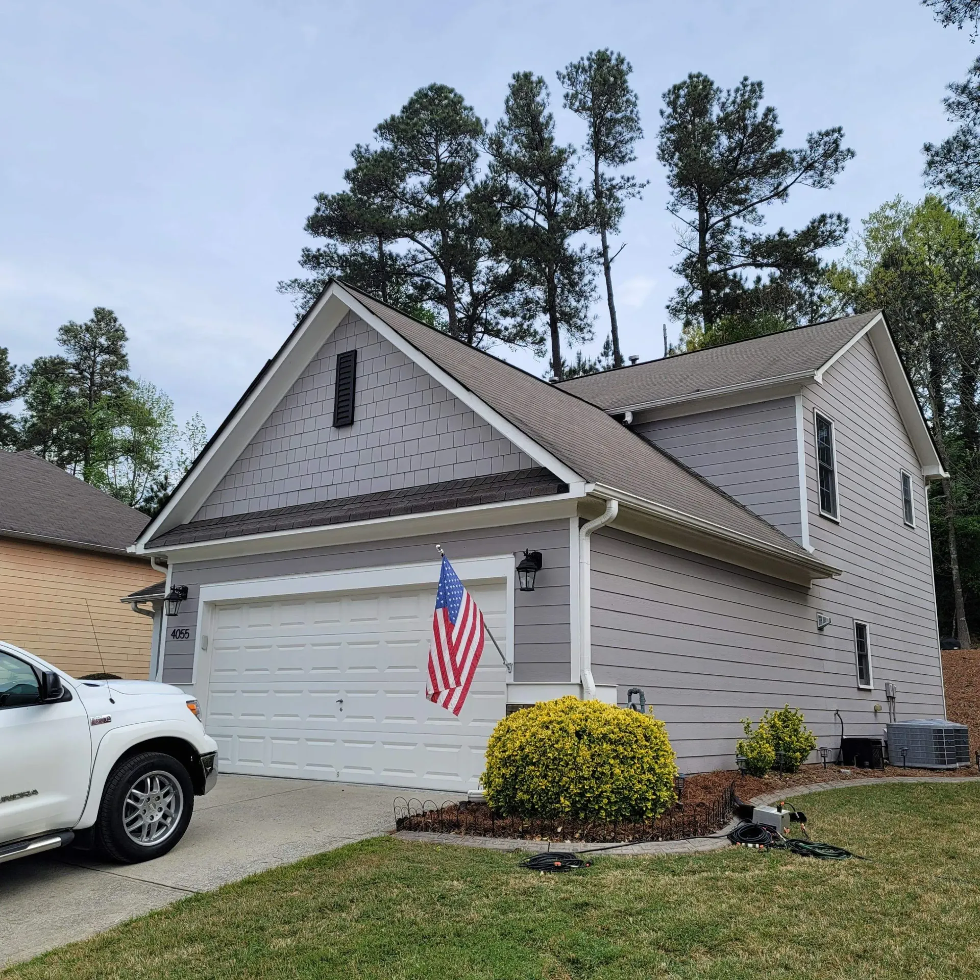 Two-story house with gray siding, white garage door, and American flag. A white truck is parked in front.