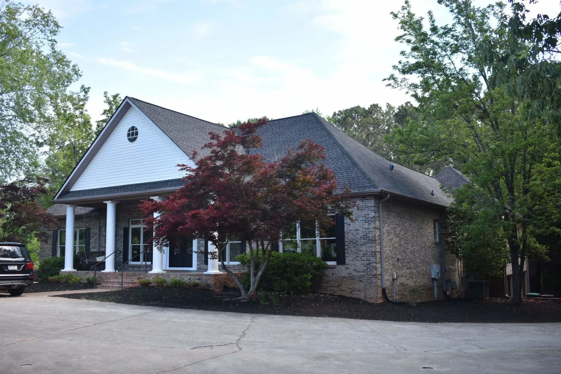 Commercial building with stone and white facade; trees and a car in the foreground.