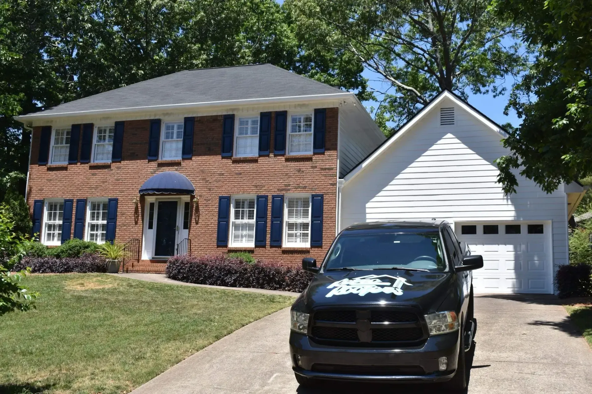 Two-story brick house with blue shutters, attached white garage, and black truck parked in the driveway.