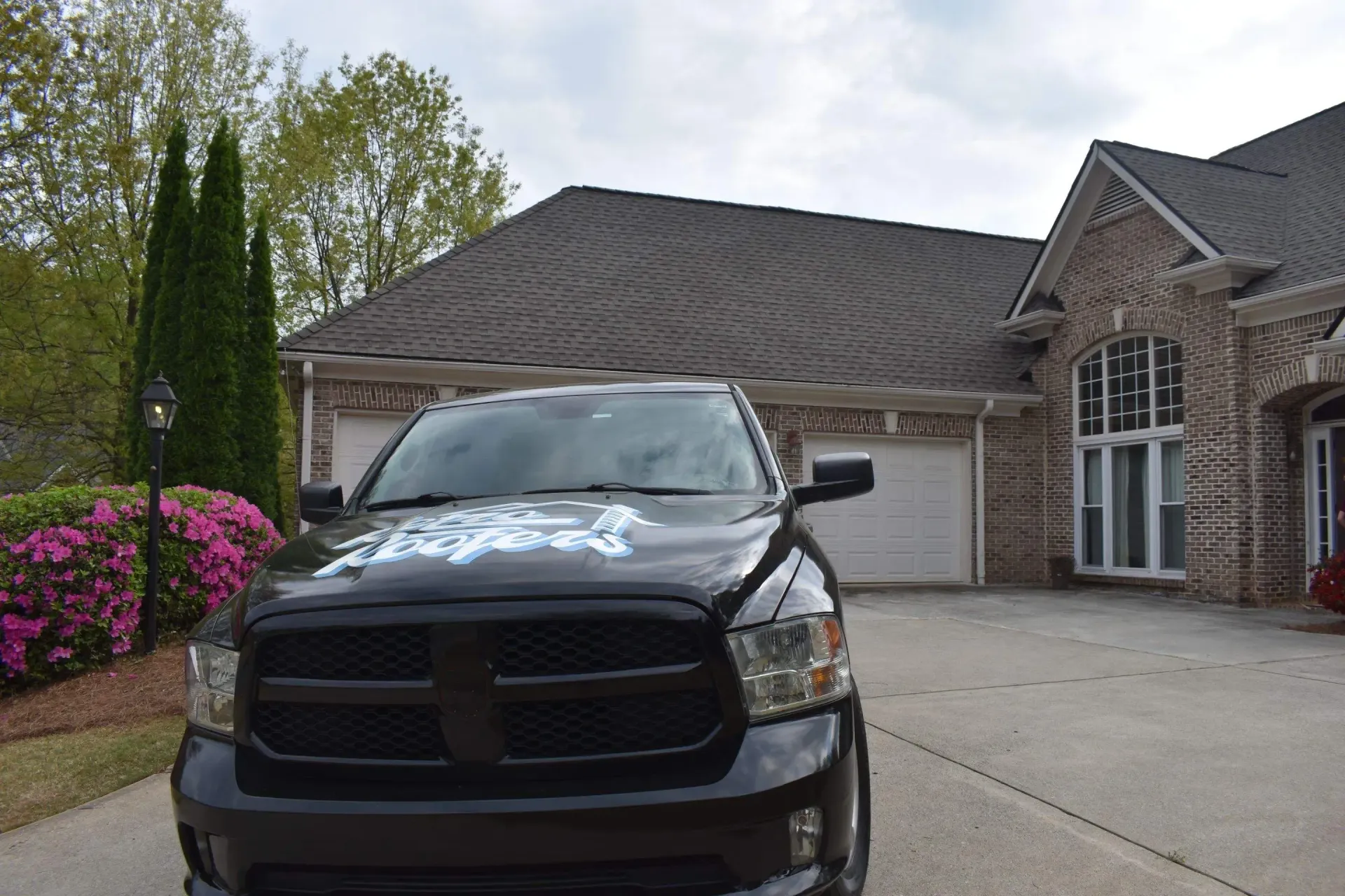 Black pickup truck parked in front of a brick house with a three-car garage and manicured landscaping.