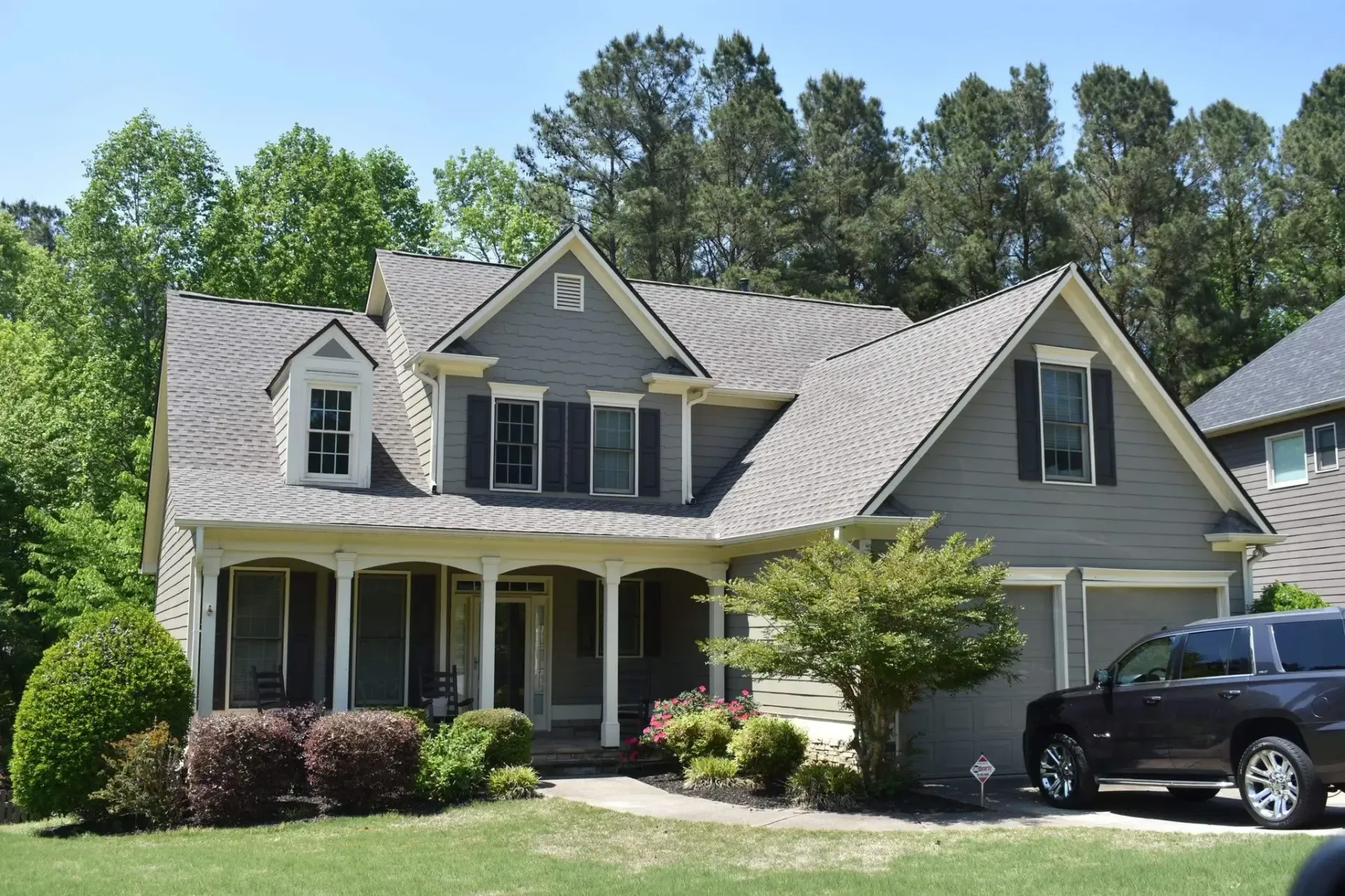 Gray two-story house with covered porch, two-car garage, and dark car parked in driveway.