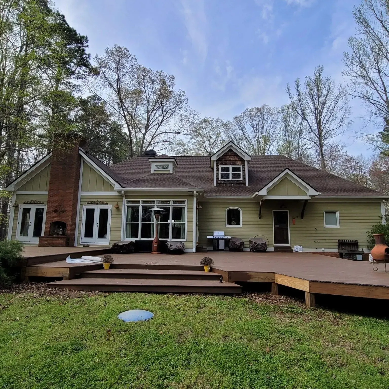 Back of a house with a large wooden deck and a green lawn, under a blue sky.