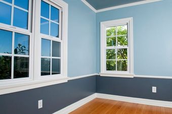 Blue and gray painted room with white trim and wooden floor, two windows.