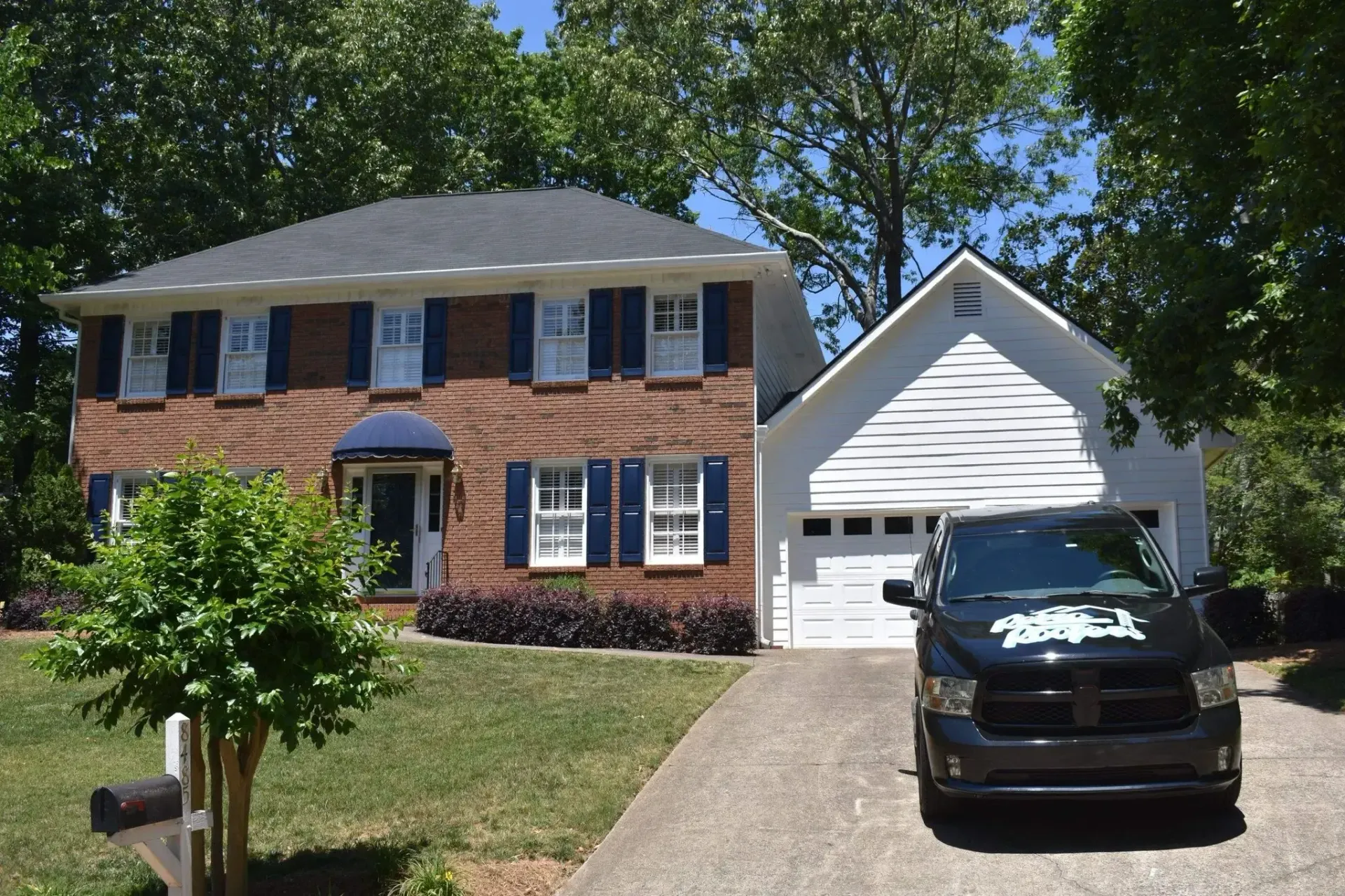 Two-story brick house with blue shutters, a white garage, and a black truck parked in the driveway.