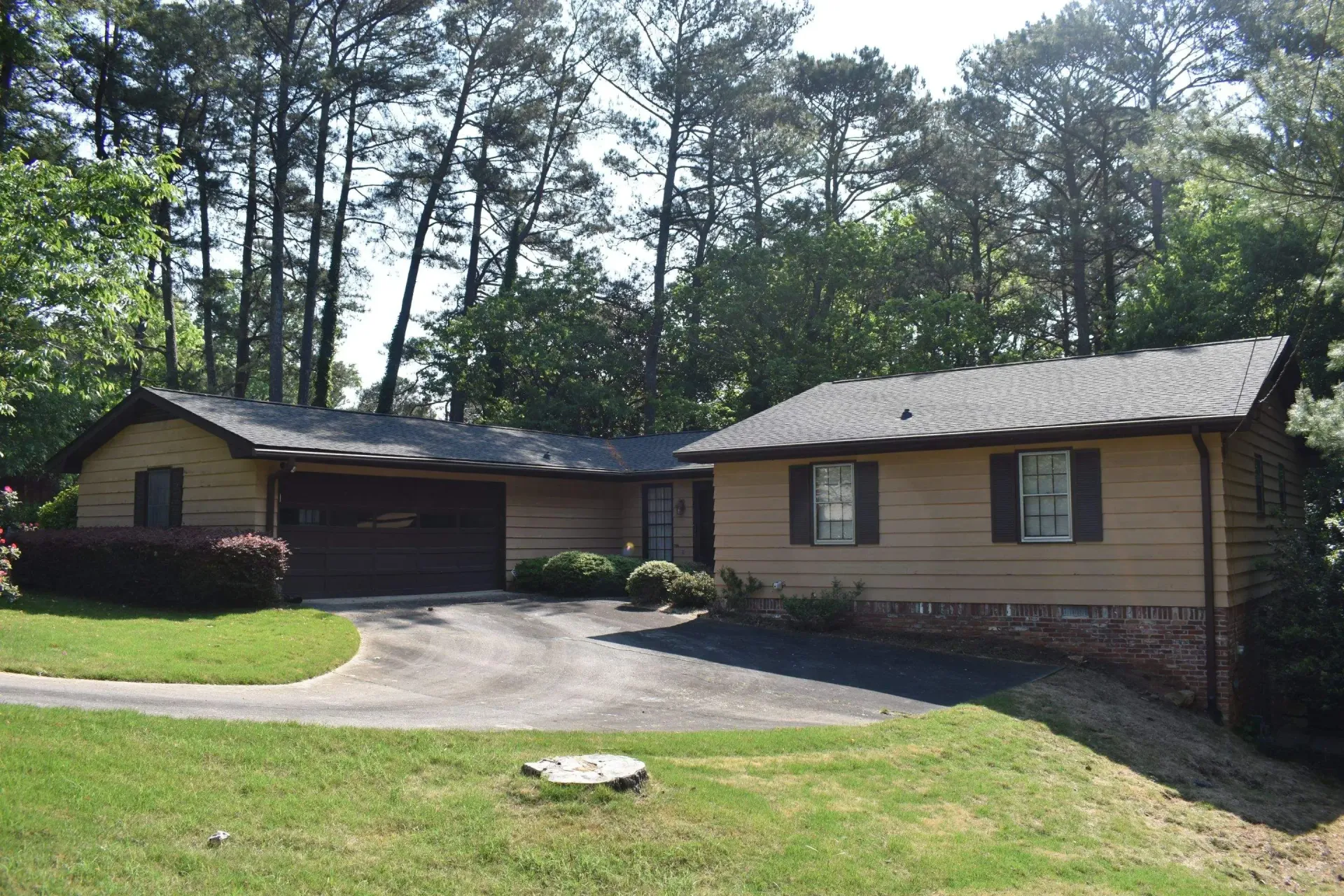 Tan house with a driveway and garage, surrounded by trees and greenery.