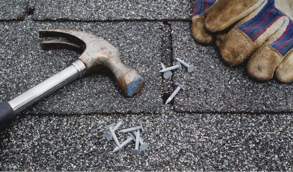 Hammer, nails, and work gloves on a dark gray shingled roof, illustrating roofing repair.