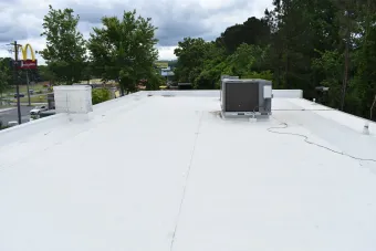 White flat commercial roof with HVAC unit, vent pipes, and a McDonald's in the background.