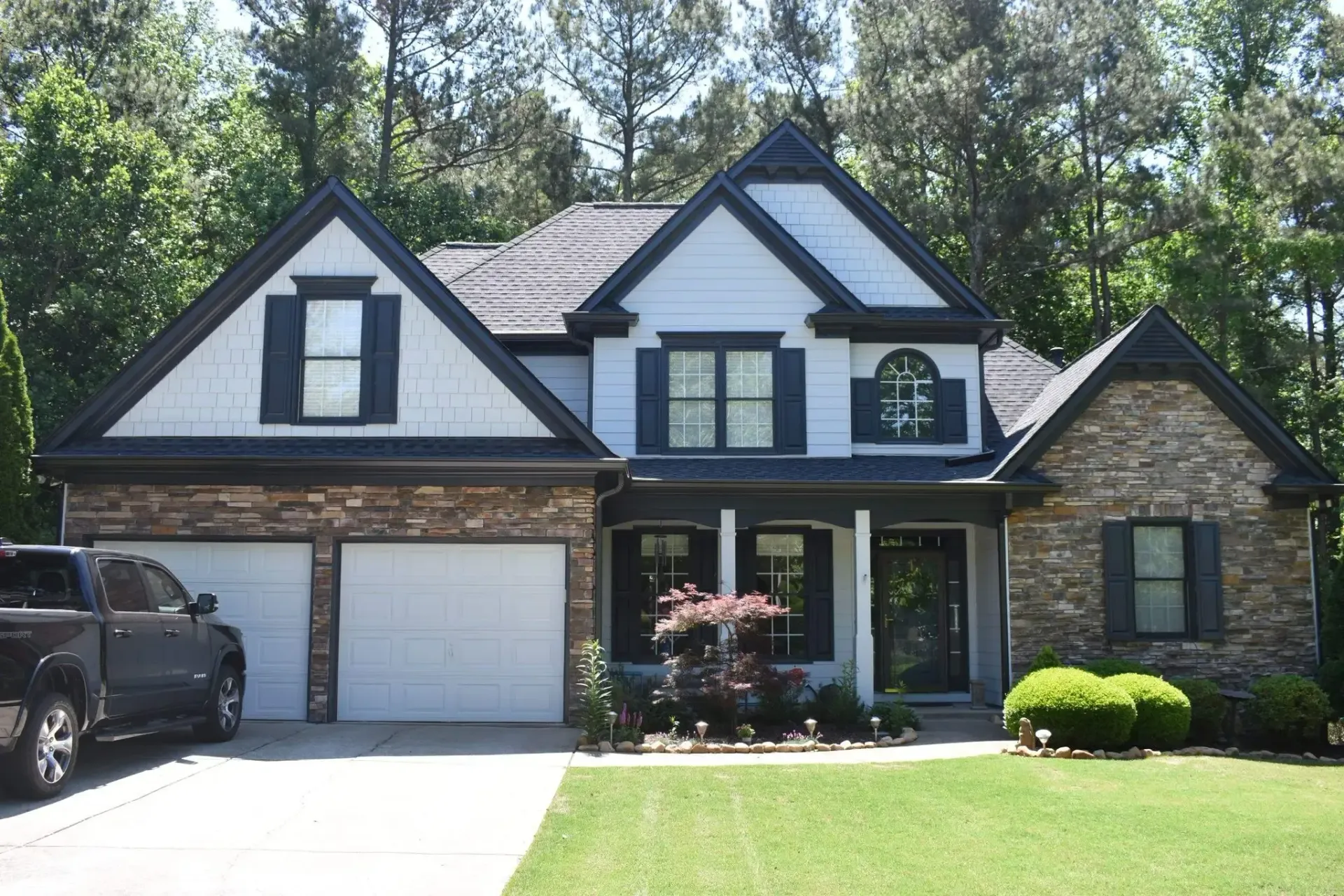 Suburban house with stone and white facade, black trim, and a black pickup truck in the driveway.