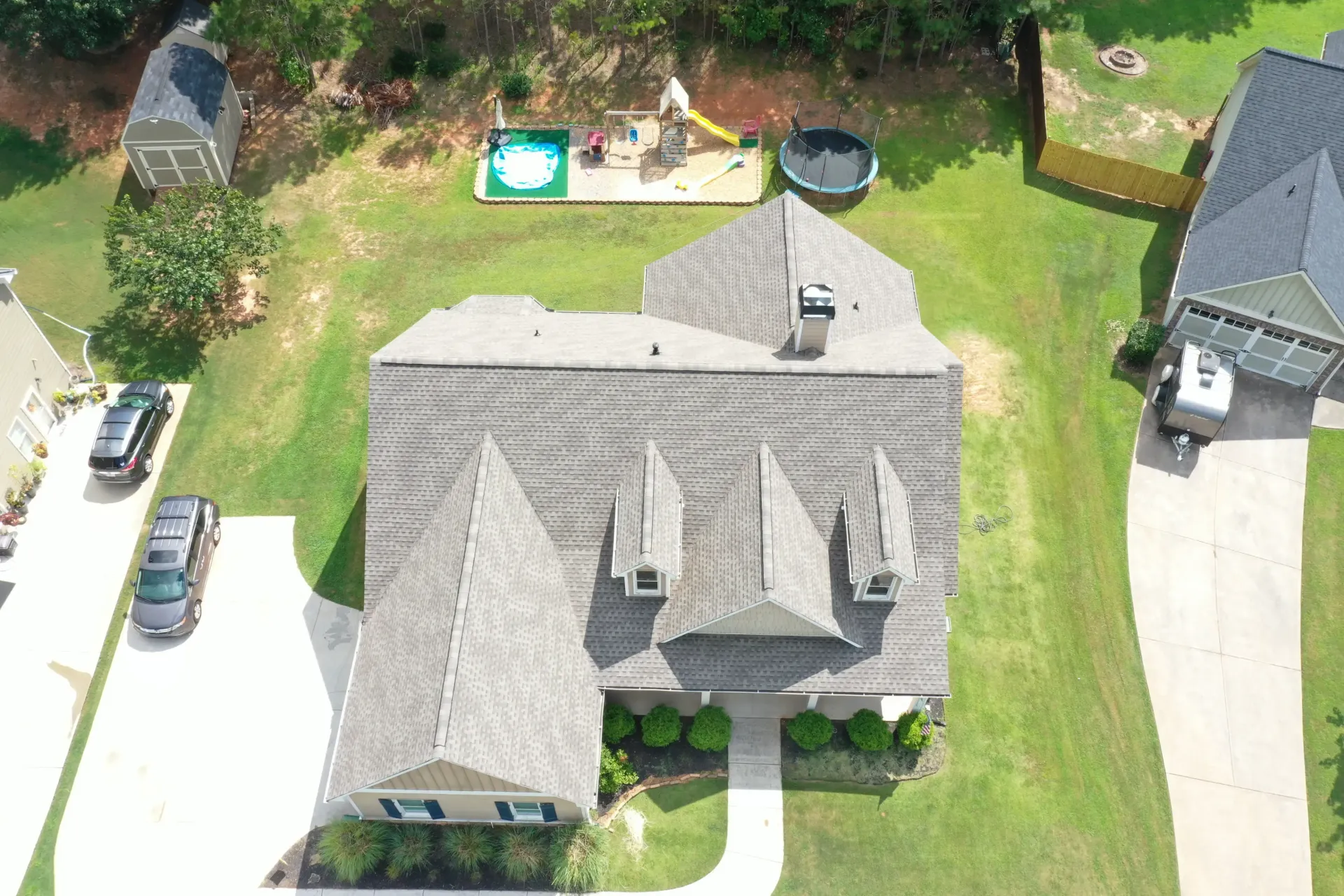 Aerial view of a house with a gray roof, driveway, and backyard with a playset and pool.