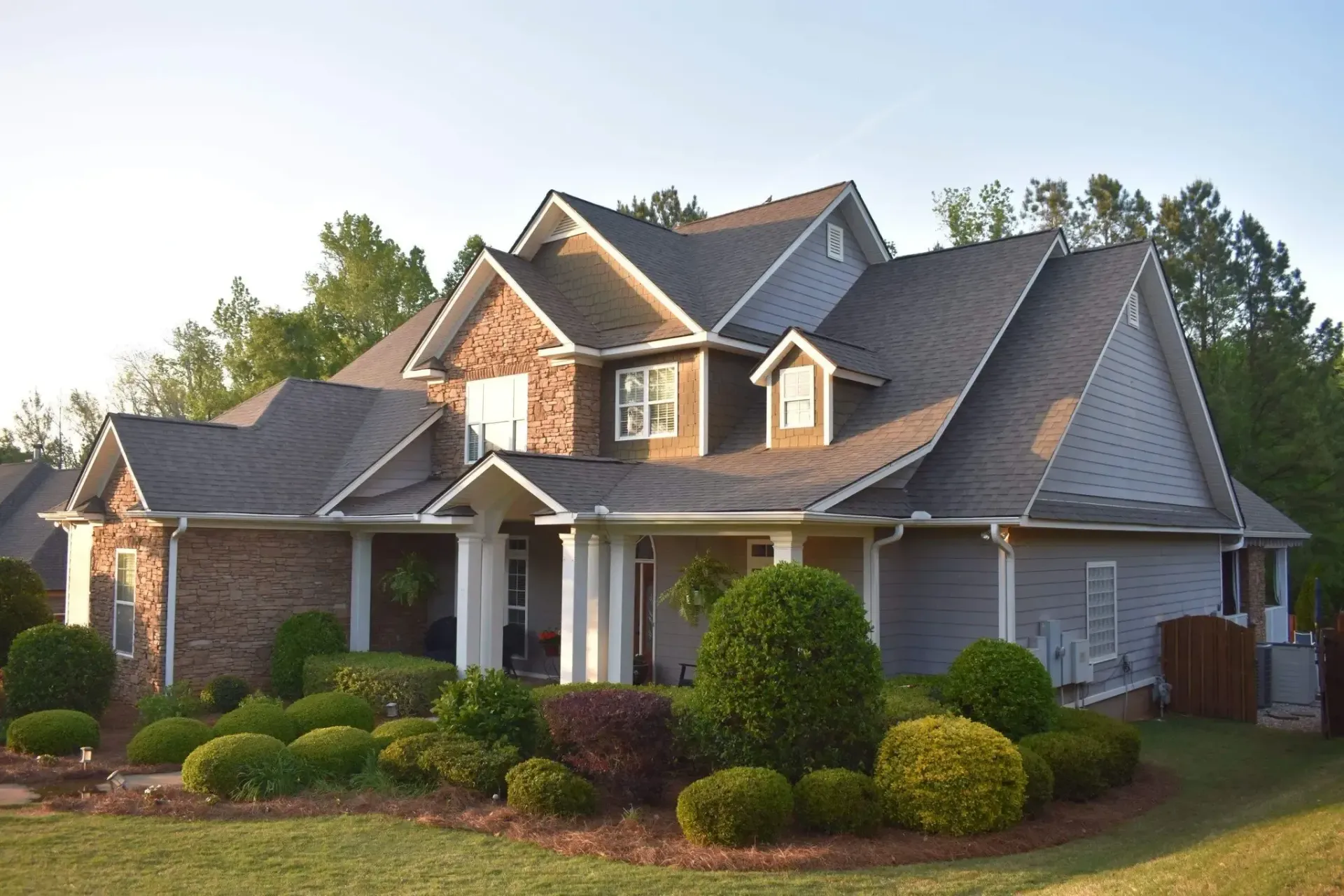 Two-story house with tan siding, brown roof, and landscaped yard.