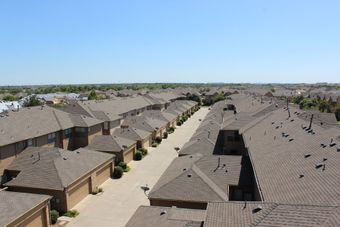 An aerial view of a residential area with rows of townhouses, brown roofs, and a clear blue sky.