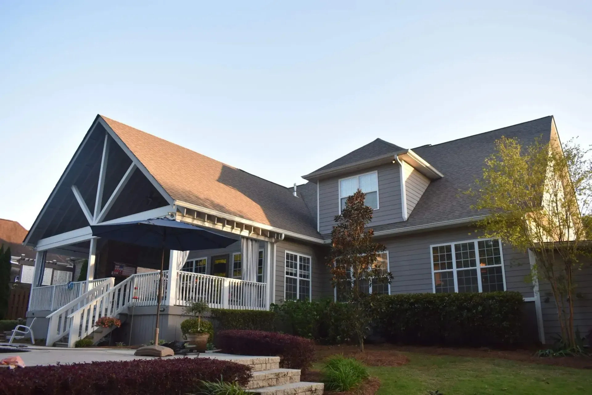 Back exterior of a two-story gray house with a deck and landscaping. Blue sky overhead.