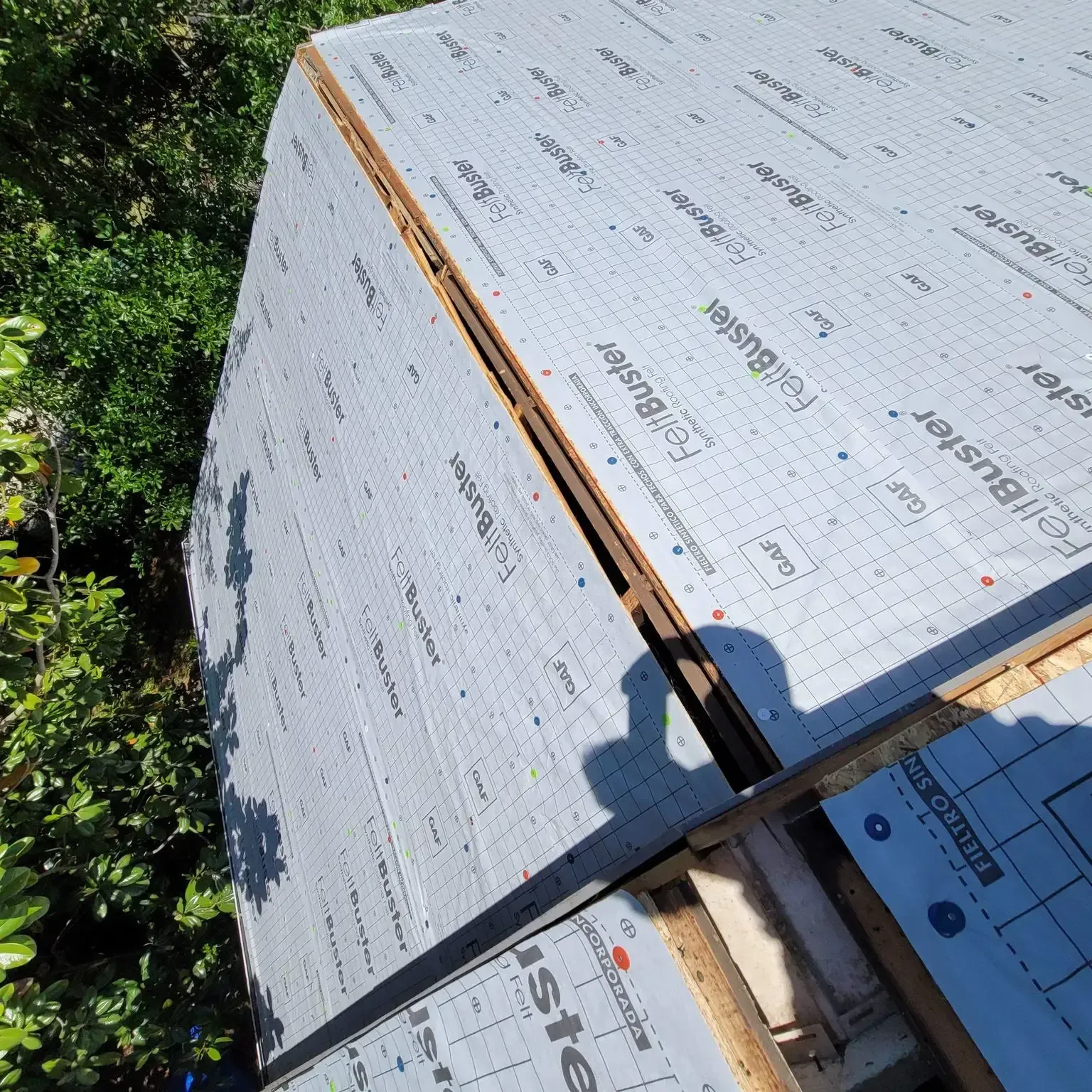 Roof construction: Felt paper underlayment on a roof, preparing for shingles. Sunlight, trees in background.