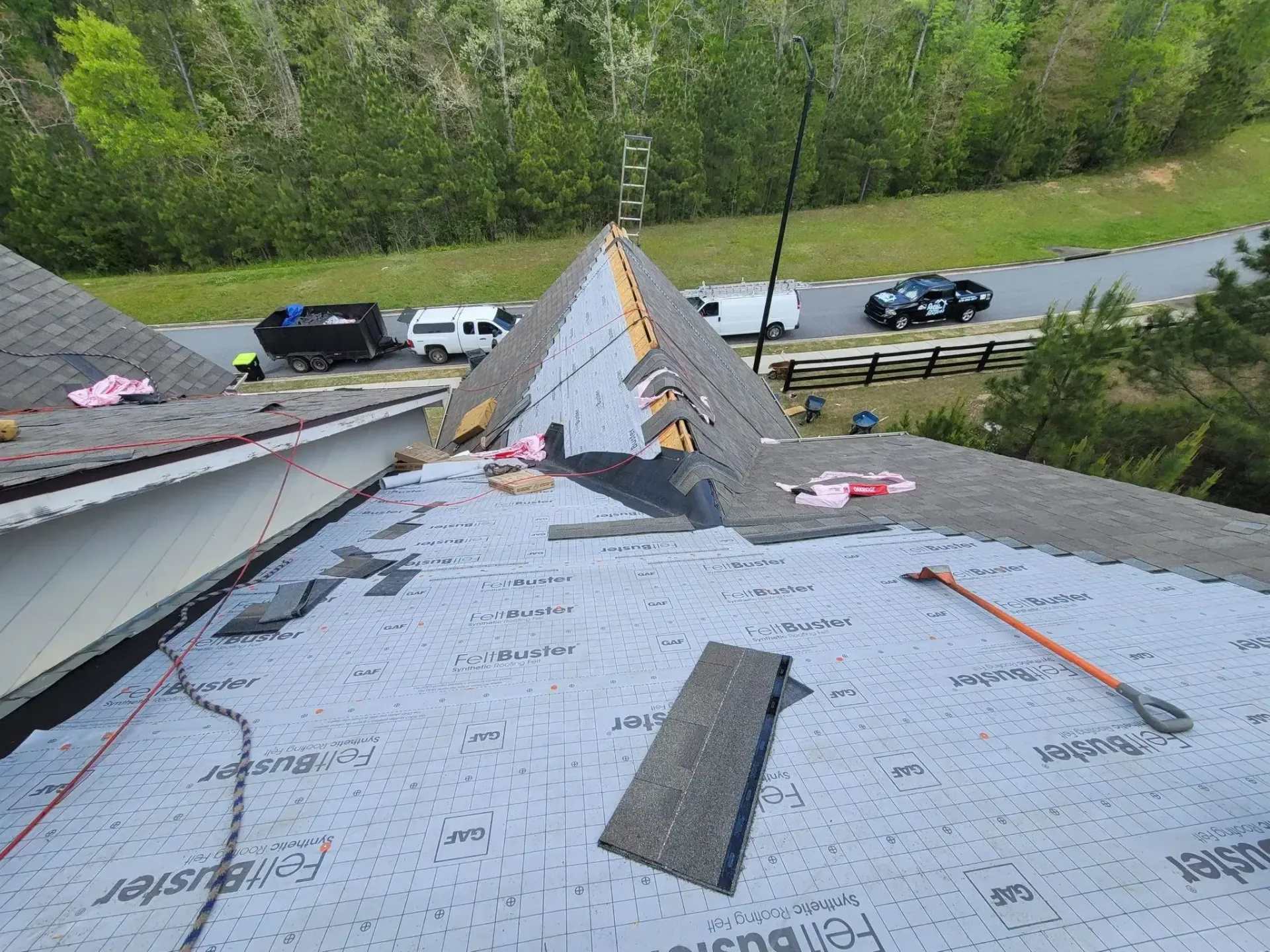 Roof being repaired with asphalt shingles and underlayment; construction vehicles in the background.