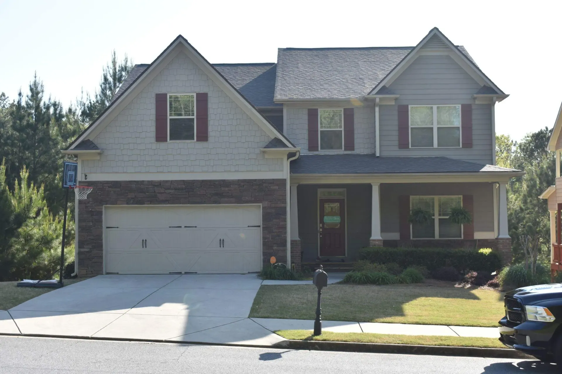 Two-story house with gray siding, brick garage, and red shutters, on a sunny day.