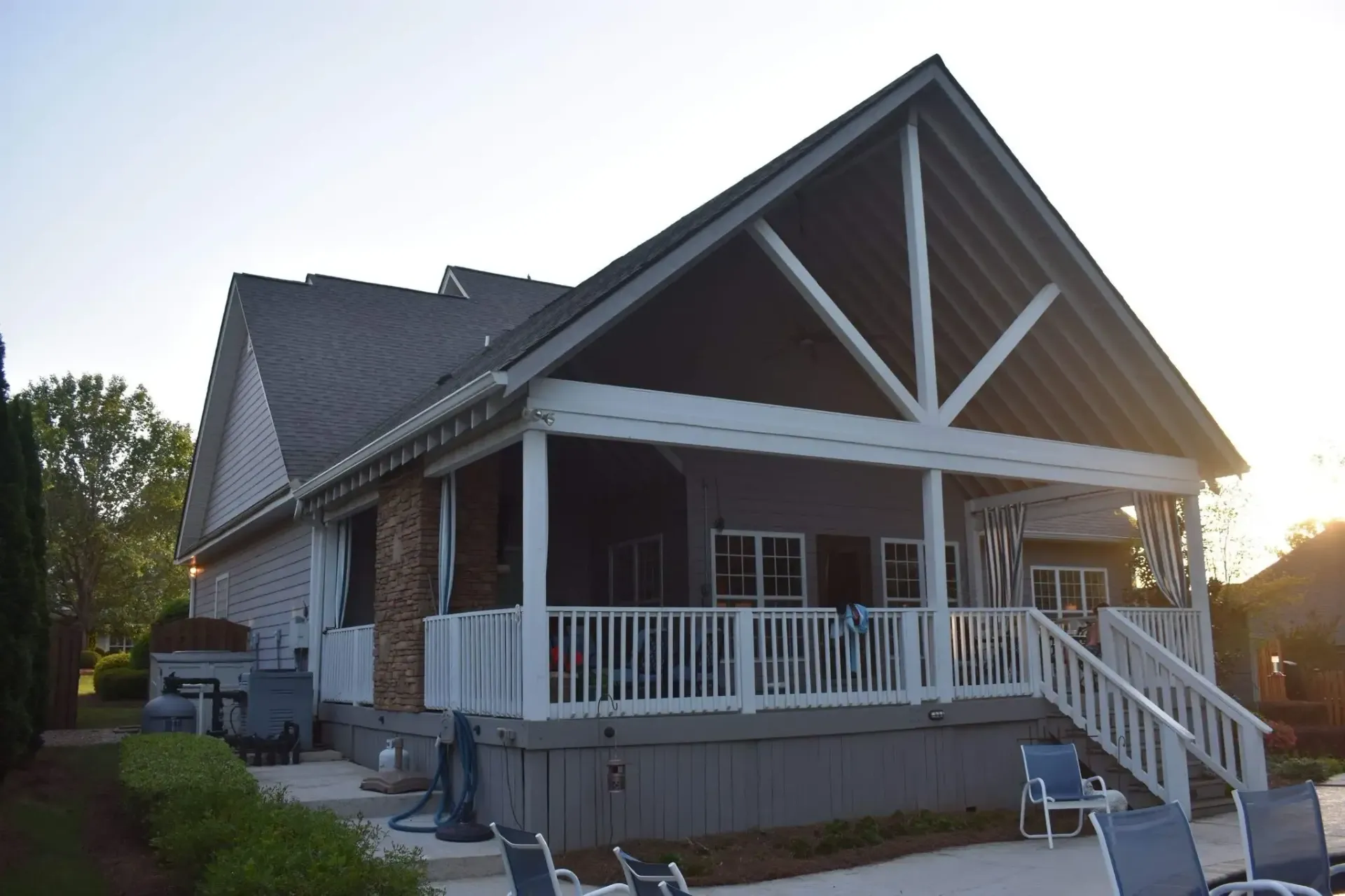 House with covered porch and stairs. White railing, gray siding, dark roof, and blue chairs visible.