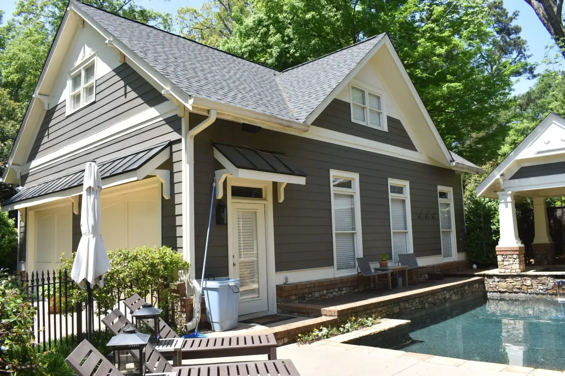 Dark gray building with white trim, near a pool. Garage door, windows, and awning are visible.