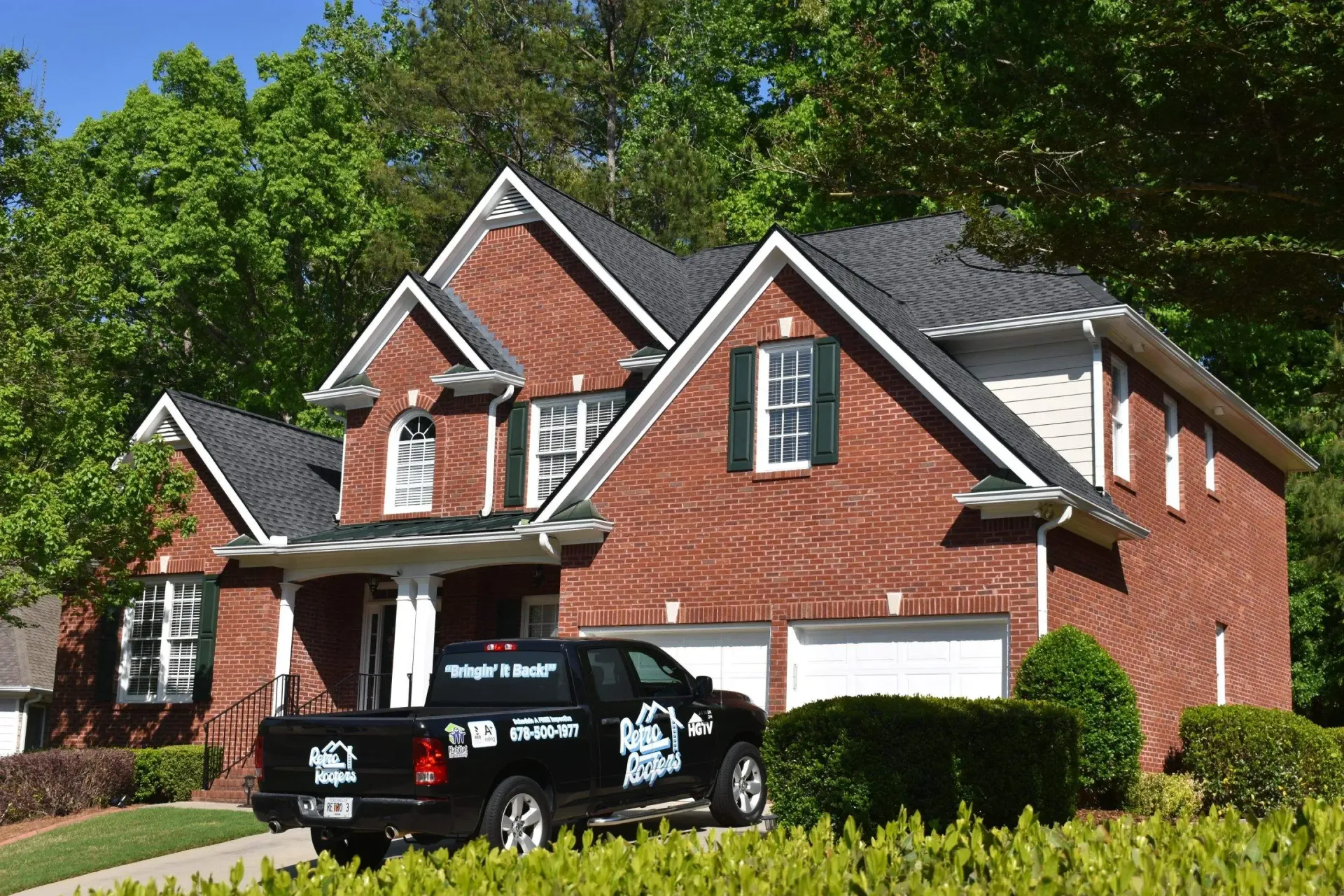 Red brick house with black roof, parked black truck in front, green foliage.