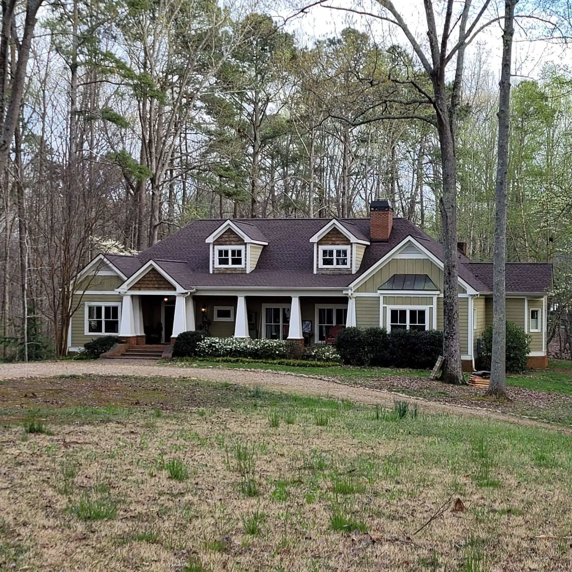 Green house with brown roof, white trim, and trees in a natural setting.
