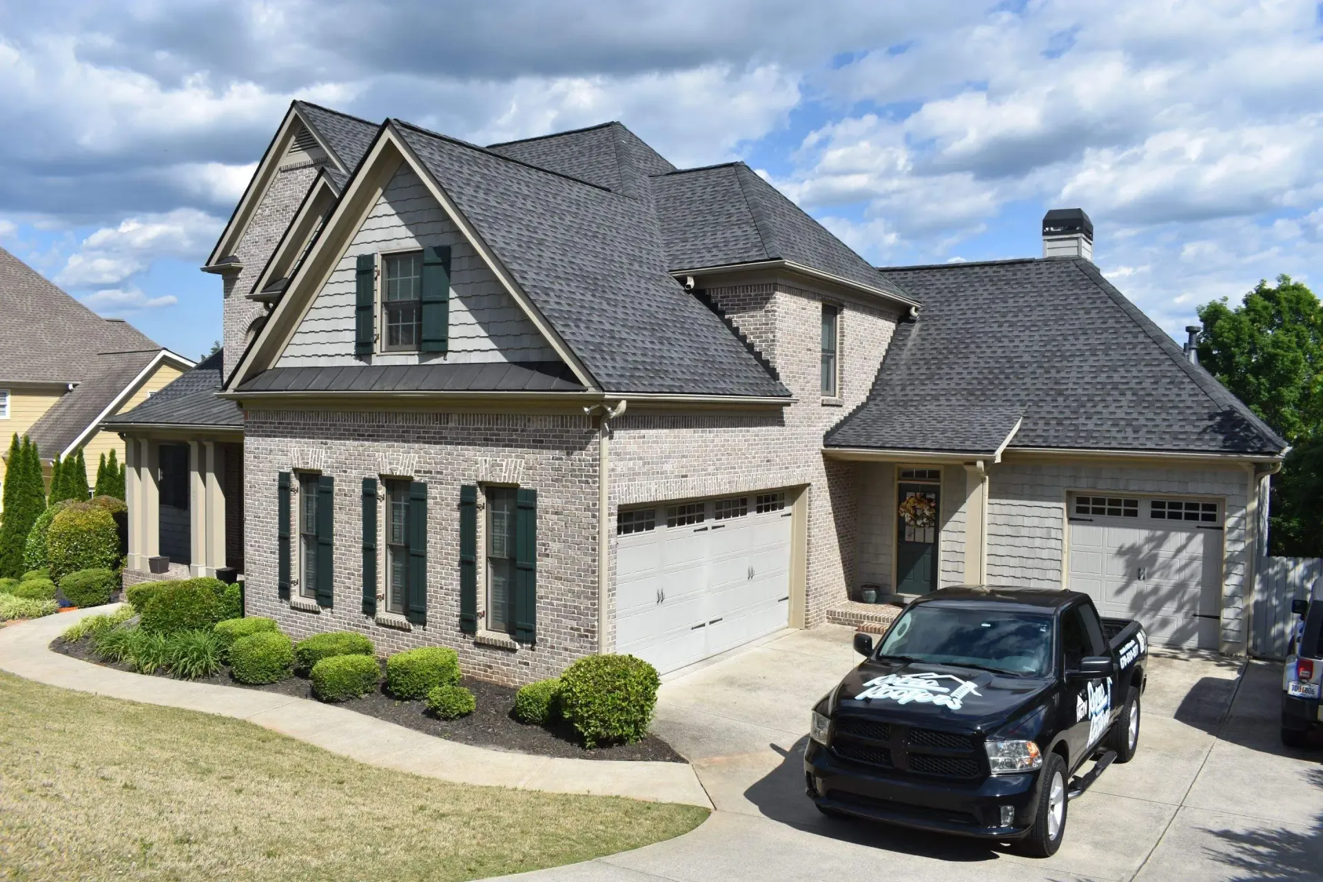 Brick house with dark gray roof, black truck in driveway, landscaping.