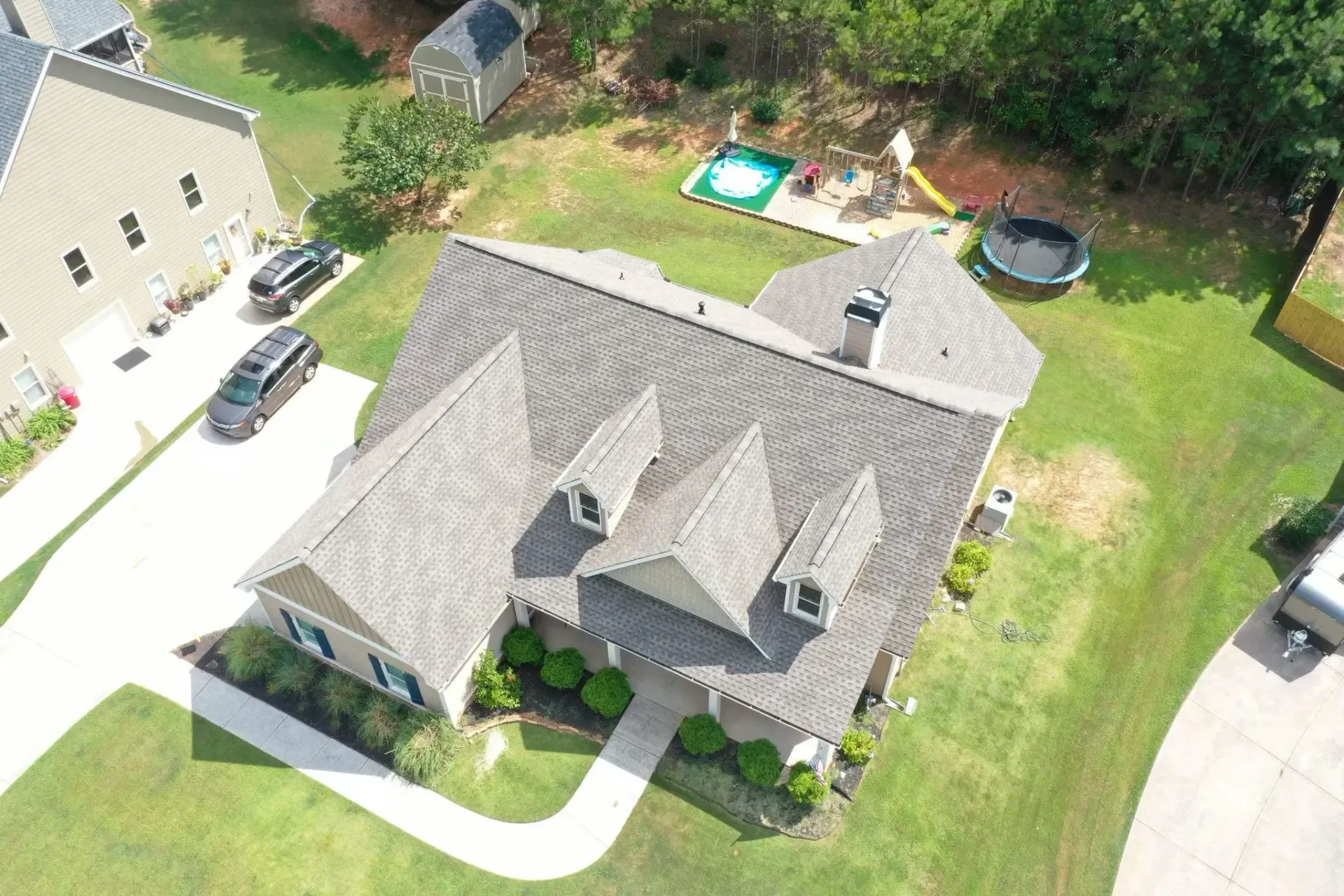 Aerial view of a house with a gray roof and driveway, surrounded by green grass.