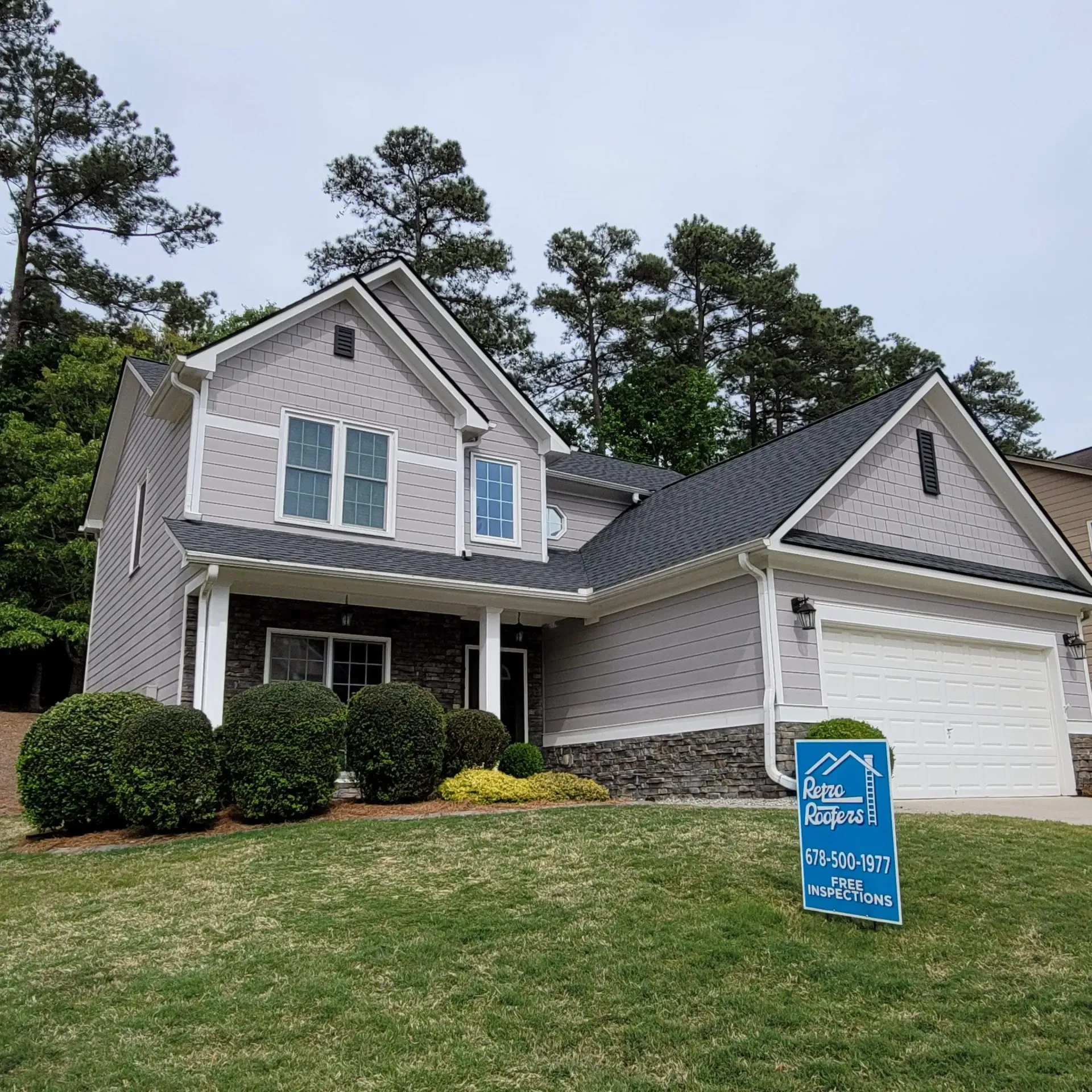 Two-story house with gray siding, black roof, and a green lawn.